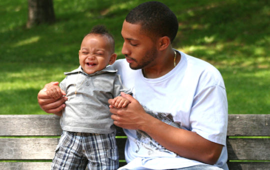 father sits on park bench with baby boy
