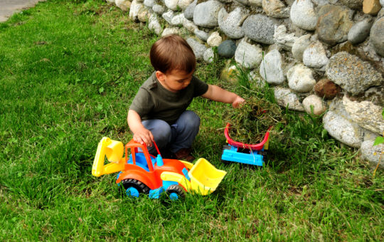 Young boy playing with toy truck in the grass.