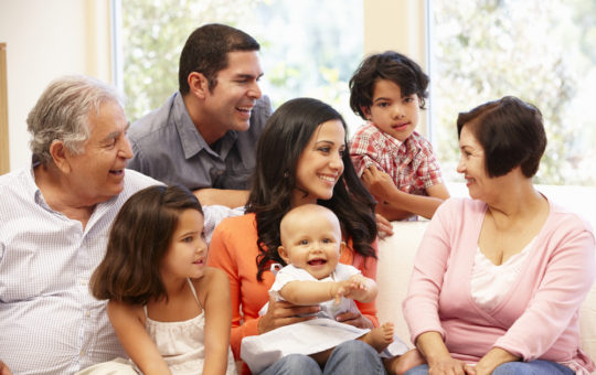 Hispanic family sitting on a couch, includes grandfather, grandmother, father, mother, boy,girl and baby