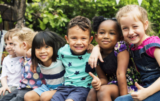 Six diverse children with arms around each other smiling