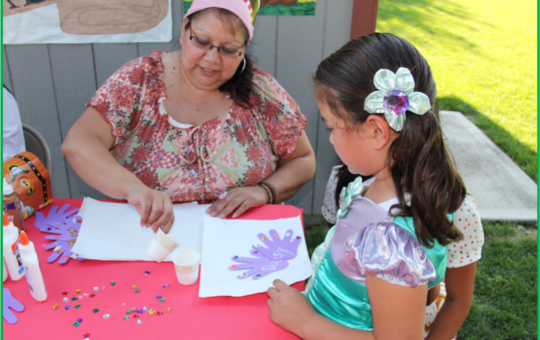A WOMAN HELPS A CHILD COLOR AT A FESTIVAL