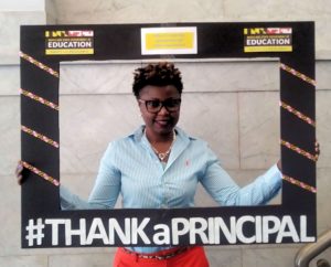 A female teacher holds up a handmade frame with the hashtag #ThankaPrincipal
