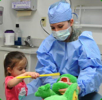 A dentist helps a child learn how to brush with the help of a stuffed crocodile.