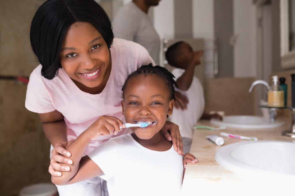 Smiling mother with daughter brushing teeth in bathroom at home
