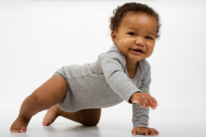 A baby in a gray onesie is crawling and smiling.