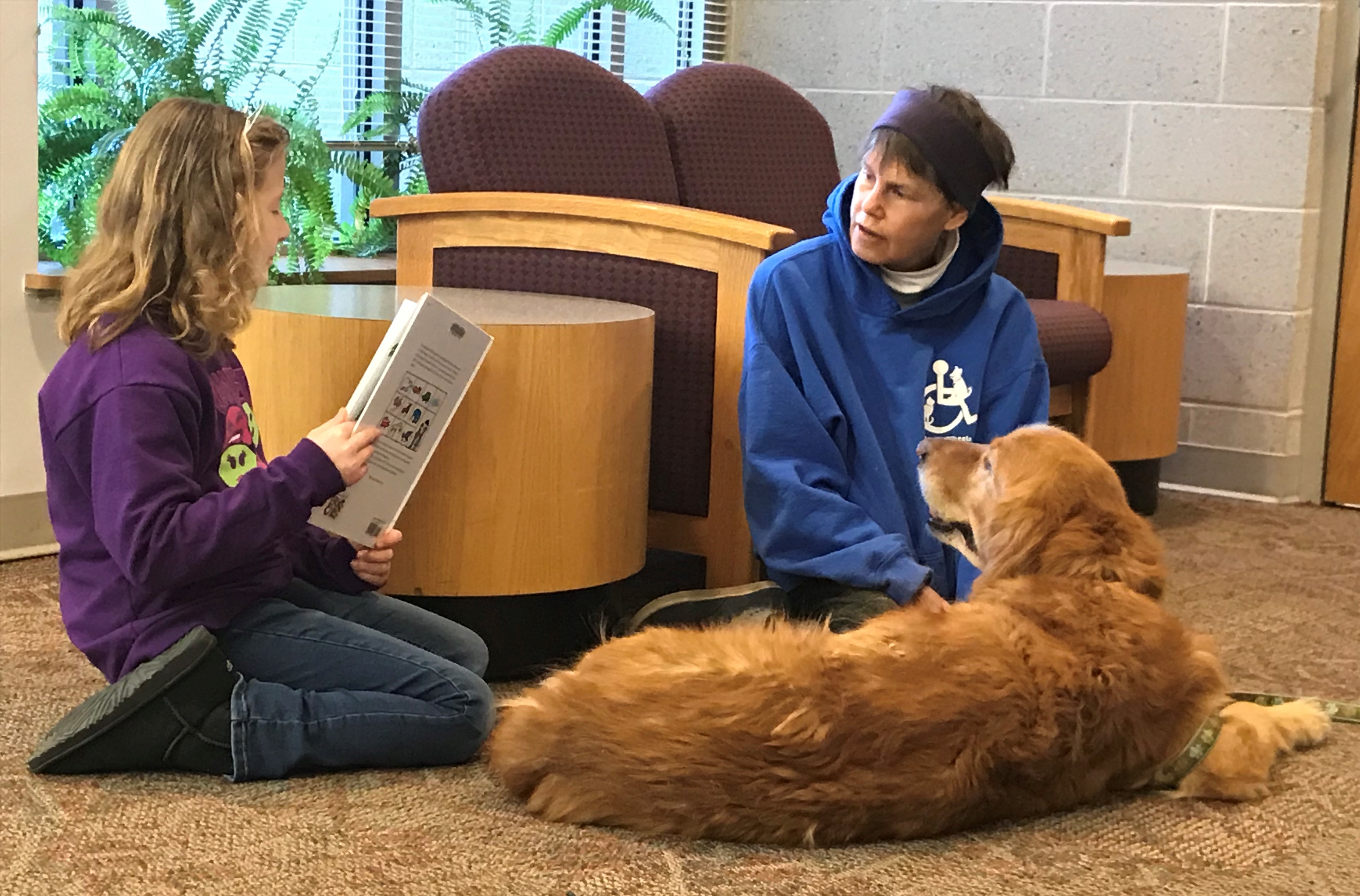 A girl reads a library book to a golden retriever