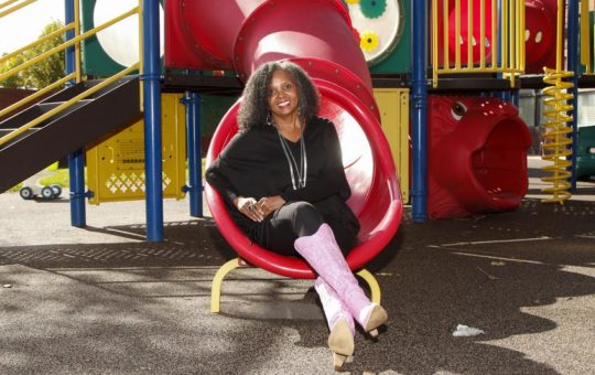 Educational expert and leader Dr. Rosemarie Allen sits at the bottom of a slide on a playground.