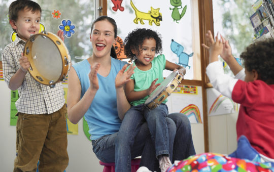 Young teacher with children playing music in classroom