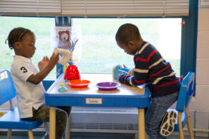 Two preschool-aged boys play with pretend kitchen items together at a table