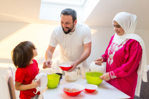 A mother, father and young child prepare food together at a table