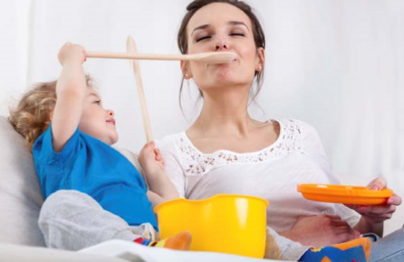 Child playing with mother by holding a wooden spoon up to her mouth