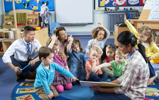 a group of children sitting on the floor with three adults for circle time in a child care program