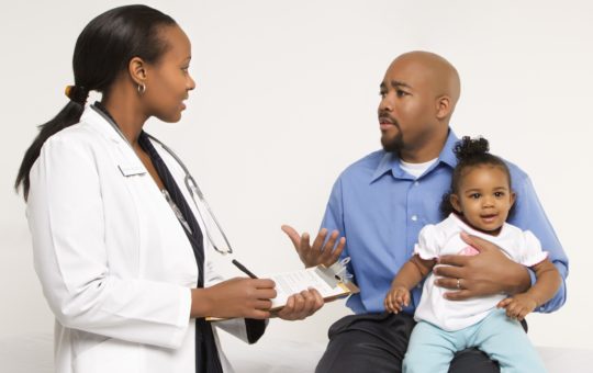 African American father with toddler daughter in his arms talking to female doctor