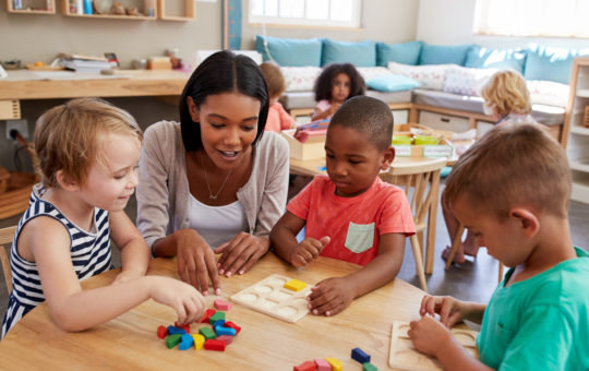 Teacher And Pupils Using Wooden Shapes In Montessori School