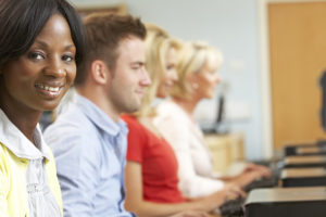 A smiling woman sits at a computer alongside three colleagues during a training class.