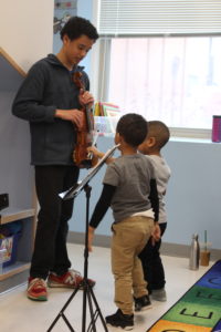 young man shows two young boys his violin