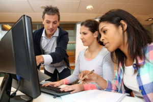 Male teacher leaning over computer screen with two female students