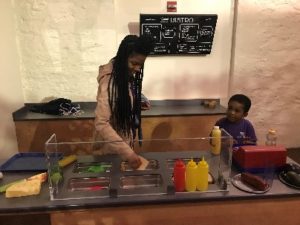 A young boy and a teacher make a sandwich at an exhibit at a children's museum