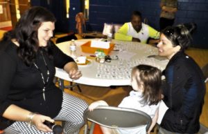 teacher sits at table with little girl and mother