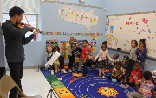 Young man plays violin to a group of young children at a child care center