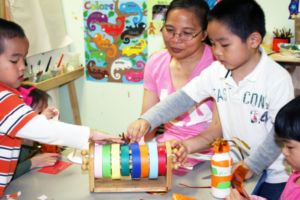 teacher sits at table with three children doing crafts with colorful tape
