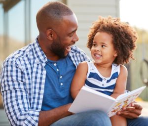 Father and daughter sit together with a book laughing