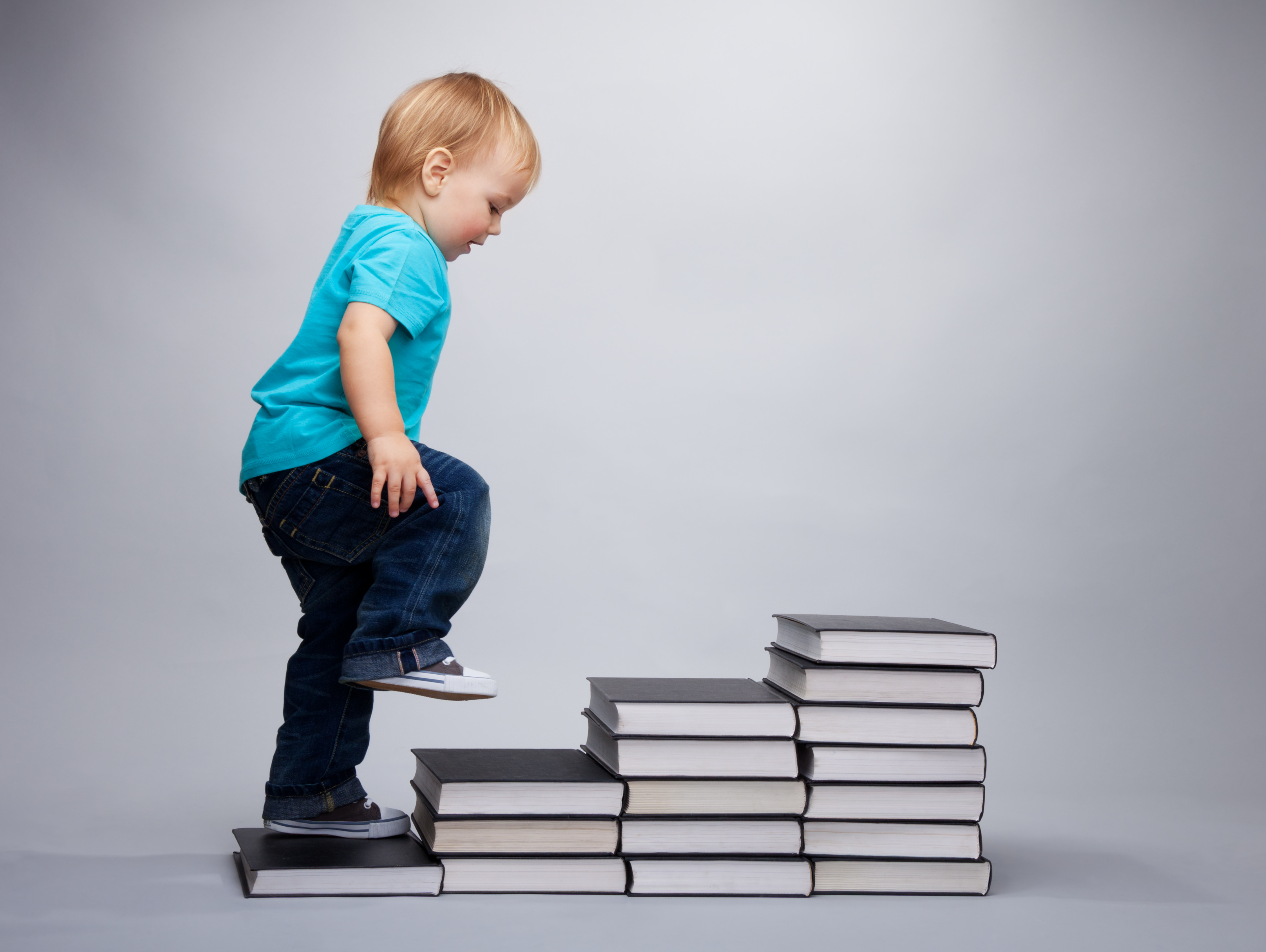 Toddler boy walking up a books lined up like stairs