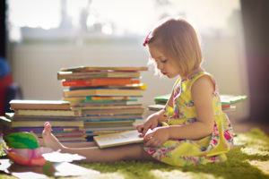 young girl in yellow sundress reads a book surrounded by books