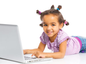 young african american girl lays on her stomach with her hands on a laptop keyboard