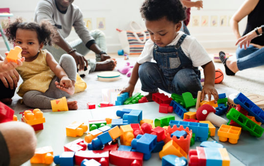 Young african american boy squats on the floor playing with large lego blocks