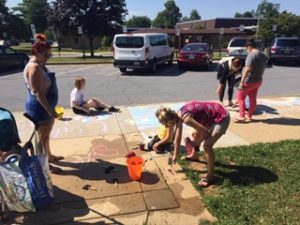 Adults and children draw on a sidewalk with chalk during a STEM day