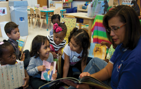 teacher sits on the floor with 6 children holding books in a child care setting
