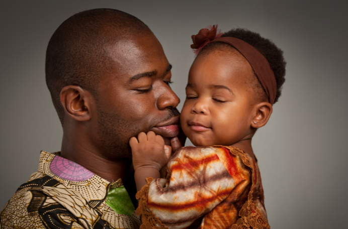Man wearing african print shirt holds and kisses toddler with their eyes closed