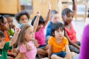 Children in learning environment raising their hands.