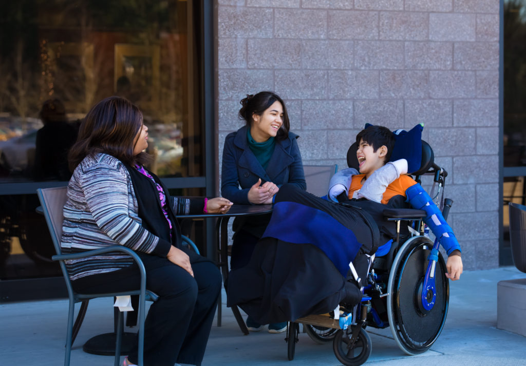 two adults sit at table with a young boy in a wheelchair