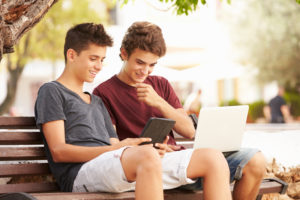 two teenage boys sit on bench looking at tablet