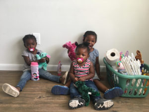 Three little girls sitting on the floor with stuffed animals.