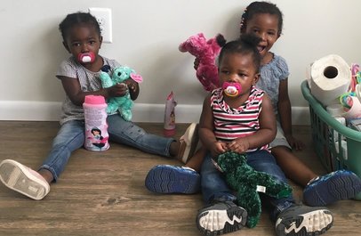 Three little girls sitting on the floor with stuffed animals.