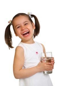 Little girl with pigtails holding a glass of water.