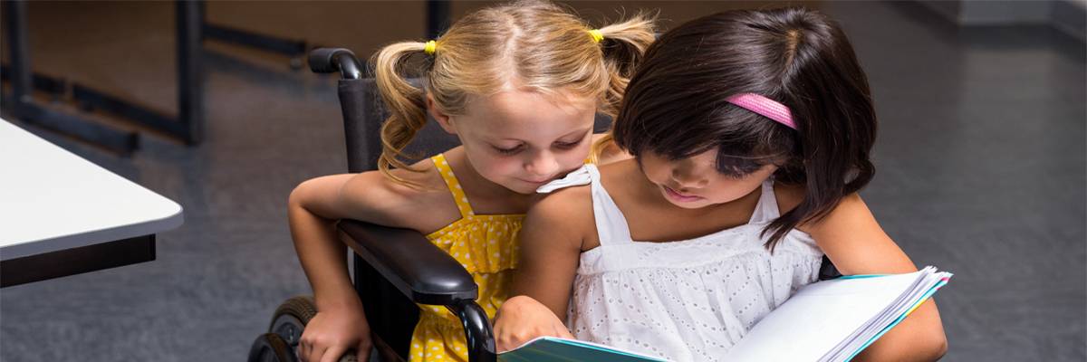 Cute girls sitting on wheelchair reading book in class room